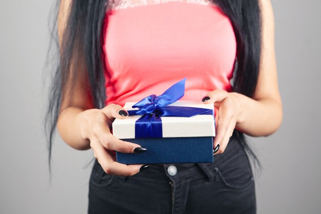 Chica joven con caja de regalo sobre fondo gris