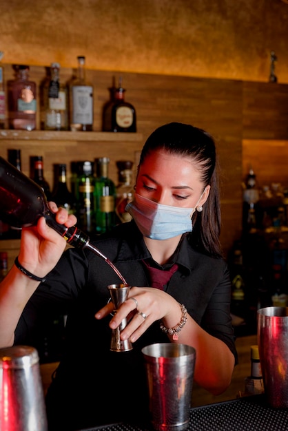 Chica joven camarero con máscara preparando cócteles en una barra de bar. concepto de trabajo
