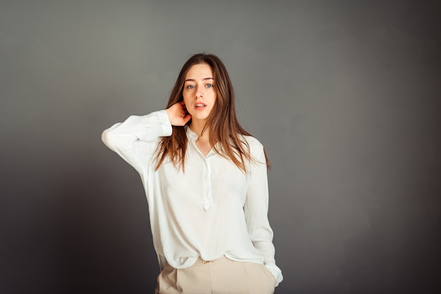 Chica joven en una camisa blanca en una pared gris. Mujer francesa en blusa blanca contra una pared de paredes grises. Sin retoques. Sin maquillaje.