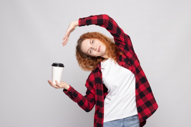 Chica joven en una camisa a cuadros con un vaso de café apunta a la información