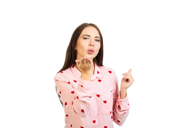 Chica joven en una camisa rosa con corazones envía un beso de aire aislado sobre un fondo blanco.