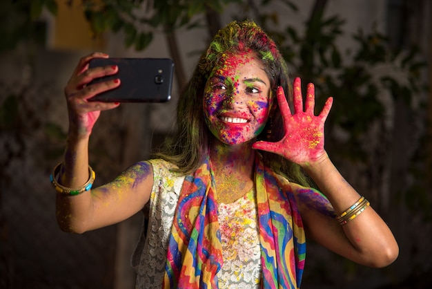 Chica joven con cara colorida tomando selfie con smartphone en festival de Holi