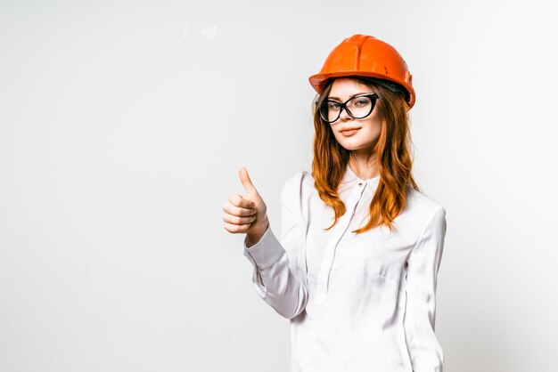 Chica joven en casco de construcción naranja mostrando el pulgar