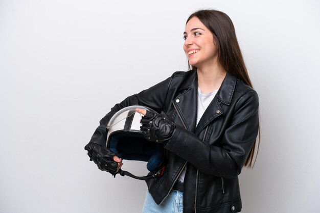 Foto chica joven con un casco de motocicleta aislado sobre fondo blanco apuntando con el dedo al costado y presentando un producto