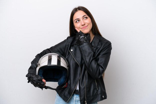 Chica joven con un casco de motocicleta aislado sobre fondo blanco mirando hacia arriba mientras sonríe