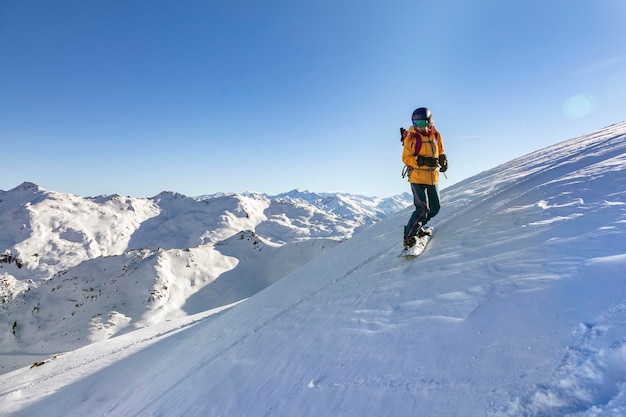 Chica joven con chaqueta amarilla y casco oscuro brillante está montando una tabla de snowboard en la zona montañosa