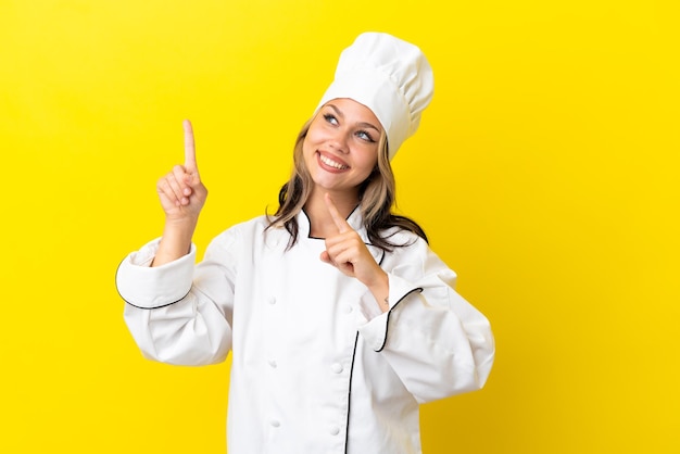 Chica joven chef ruso aislada sobre fondo amarillo apuntando con el dedo índice una gran idea