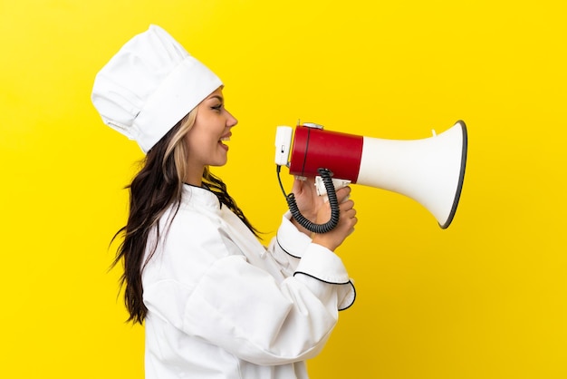 Chica joven chef ruso aislado sobre fondo amarillo gritando a través de un megáfono