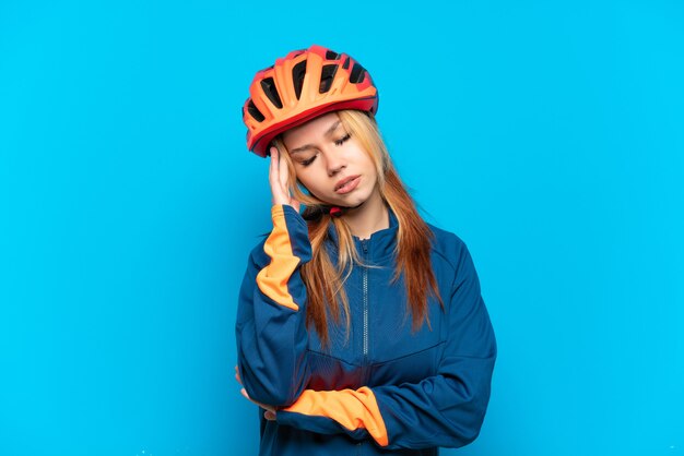 Chica joven ciclista aislada sobre fondo azul con dolor de cabeza