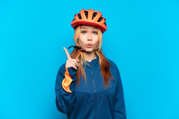 Chica joven ciclista aislada sobre fondo azul con la intención de darse cuenta de la solución mientras levanta un dedo
