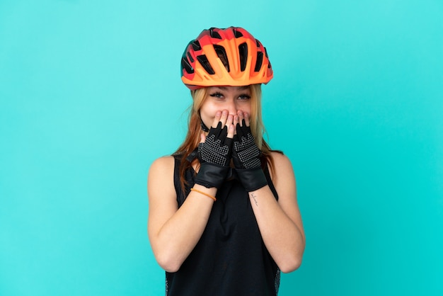 Chica joven ciclista sobre fondo azul aislado feliz y sonriente cubriendo la boca con las manos