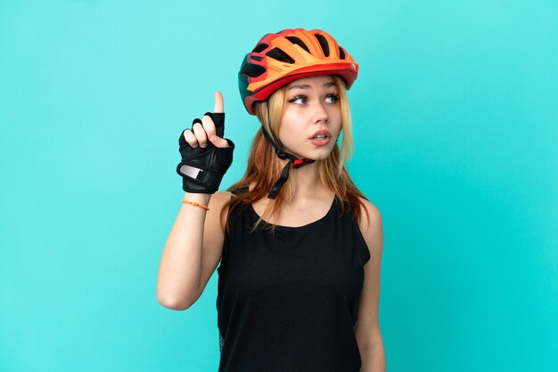 Chica joven ciclista sobre fondo azul aislado con la intención de darse cuenta de la solución mientras levanta un dedo hacia arriba