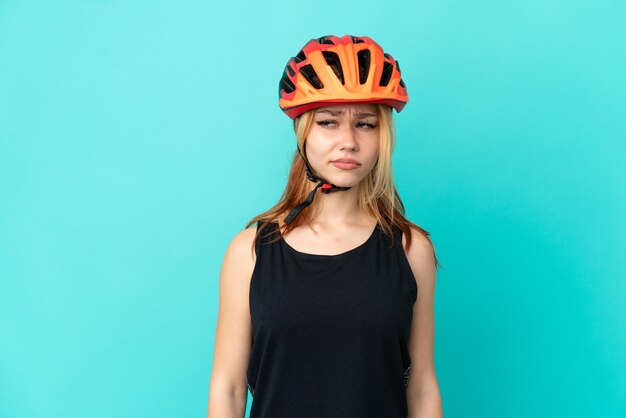 Chica joven ciclista sobre fondo azul aislado teniendo dudas mientras mira de lado