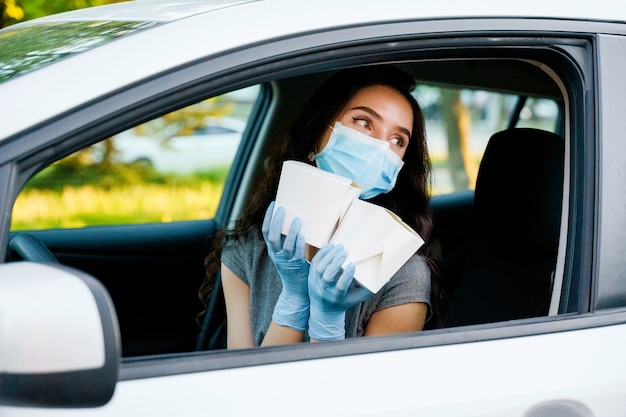 Foto chica joven en coche en guantes médicos y máscara tiene wok en caja