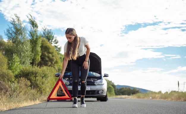 Chica joven colocando un triángulo delante del coche