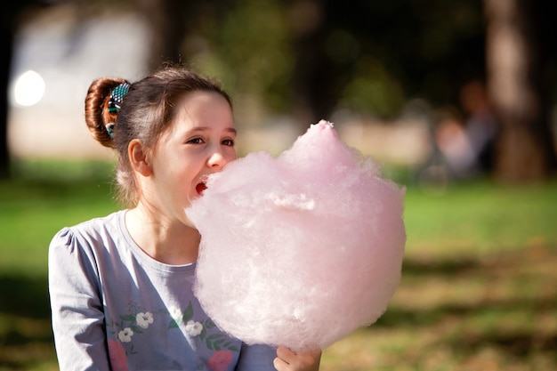 Chica joven comiendo algodón de azúcar en el parque