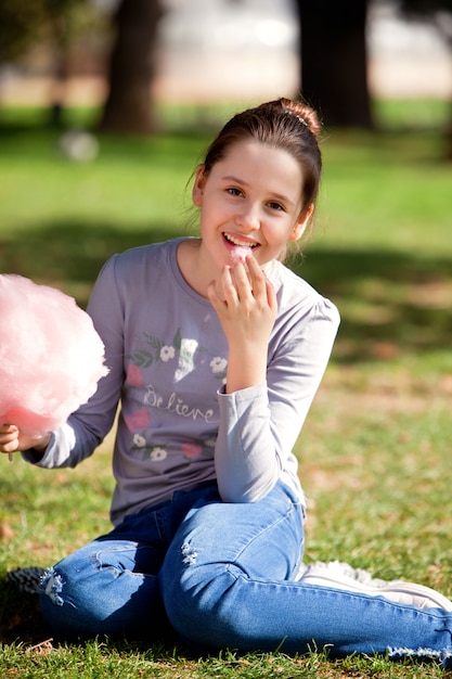 Chica joven comiendo algodón de azúcar en el parque