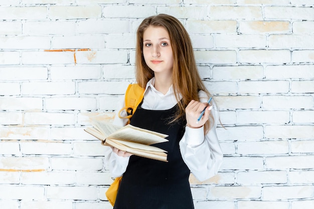 Chica joven confiada que sostiene su libro y que mira la cámara