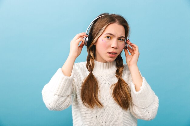 Chica joven confundida con ropa de invierno que se encuentran aisladas, escuchando música con auriculares