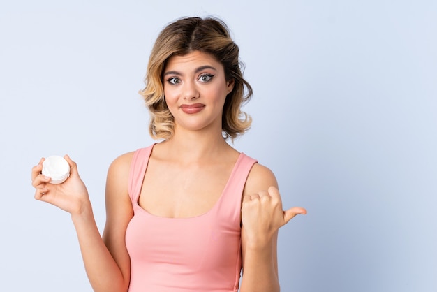 Chica joven con crema hidratante apuntando hacia el lado para presentar un producto