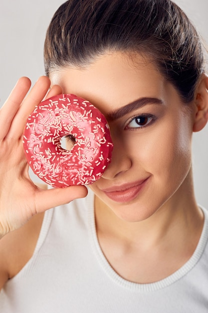 Chica joven cubrió su rostro con postre rosa. Chica morena prueba un postre. Los dulces son comida chatarra poco saludable.