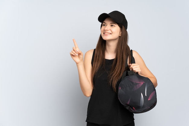 Chica joven deporte con bolsa de deporte aislada en gris apuntando hacia una gran idea