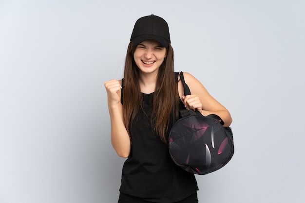 Chica joven deporte con bolsa de deporte aislada en gris celebrando una victoria en la posición ganadora