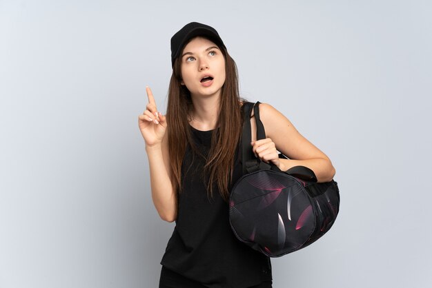 Chica joven deporte con bolsa de deporte aislada en gris pensando en una idea apuntando con el dedo hacia arriba