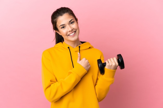 Chica joven deporte haciendo levantamiento de pesas sobre fondo rosa aislado dando un gesto de pulgar hacia arriba