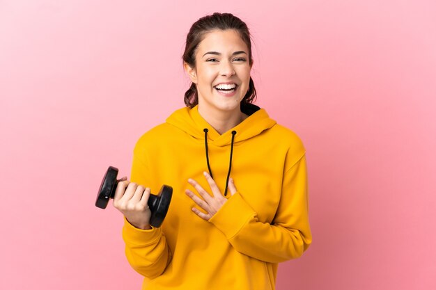 Chica joven deporte haciendo levantamiento de pesas sobre pared rosa aislada sonriendo mucho