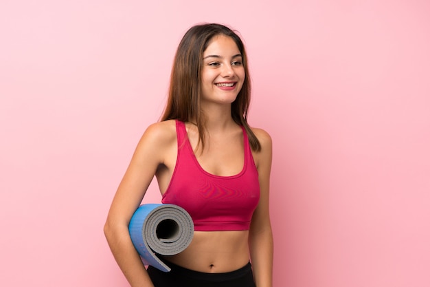Chica joven deporte sobre rosa aislado con una estera y sonriente