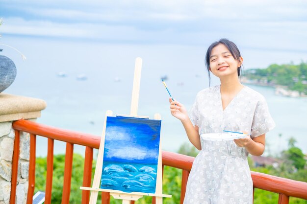 Chica joven con dibujo de pincel sobre papel de lienzo en una hermosa vista del paisaje en koh tao Tailandia