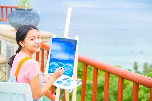 Chica joven con dibujo de pincel sobre papel de lienzo en una hermosa vista del paisaje en koh tao Tailandia