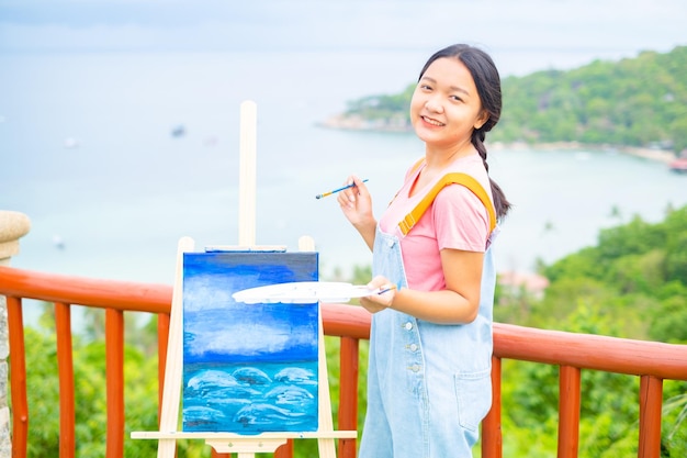 Chica joven con dibujo de pincel sobre papel de lienzo en una hermosa vista del paisaje en koh tao Tailandia