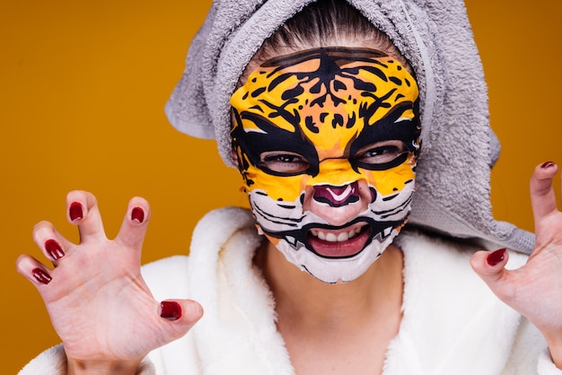 Chica joven divertida con una toalla en la cabeza gruñe, mascarilla con cara de leopardo