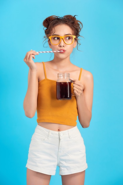 Chica joven elegante está bebiendo agua con gas sobre fondo azul.