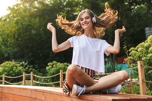 Chica joven emocionada escuchando música con auriculares en el parque al aire libre, bailando