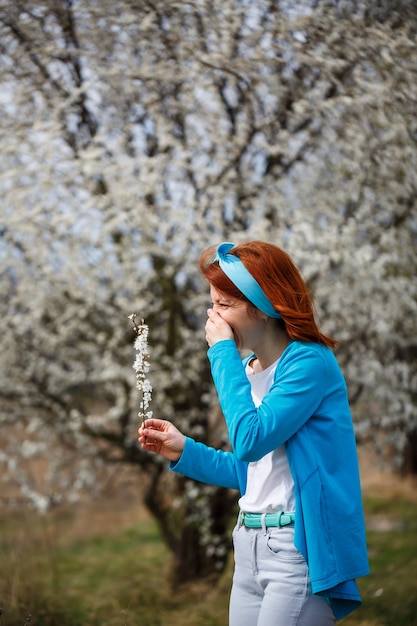 Una chica joven se encuentra en un jardín donde florecen las cerezas y los albaricoques. Ella es feliz respirando aire, flores de primavera en el fondo.