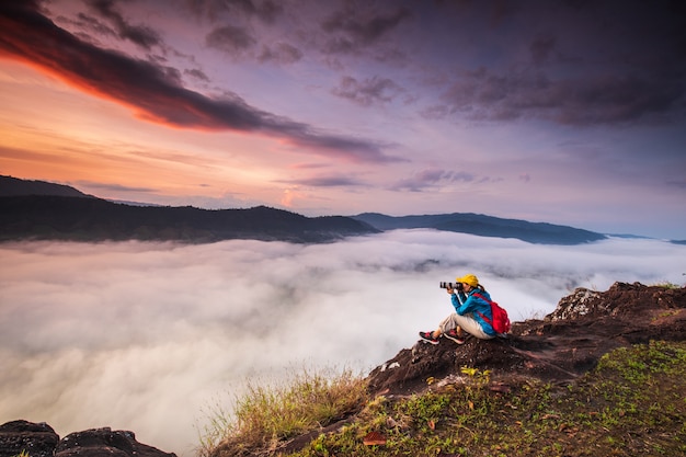 La chica joven está tomando fotos el mar de la niebla en la alta montaña.