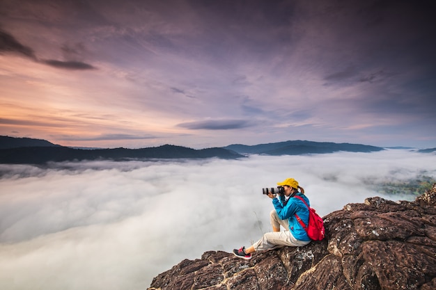 La chica joven está tomando fotos el mar de la niebla en la alta montaña.