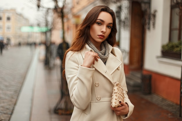 Chica joven con estilo en un abrigo de moda con un bolso de moda en la ciudad