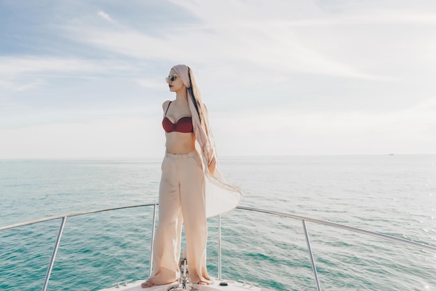 Chica joven con estilo en ropa de verano posando en su yate blanco bajo el sol disfrutando de un viaje por mar