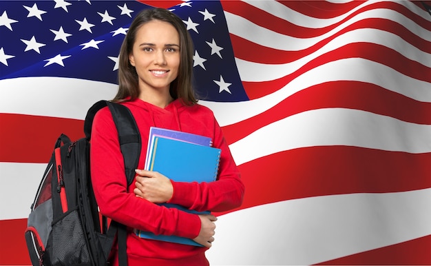 Chica joven estudiante con mochila y libros contra la bandera americana