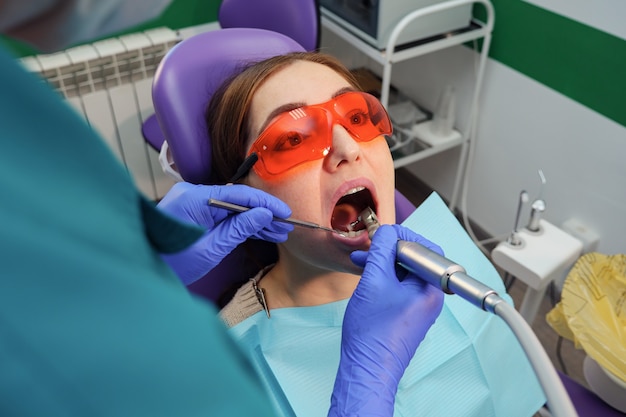 Chica joven en examen preventivo en el sillón dental del dentista. Las manos de un dentista con herramientas dentales están comprobando los dientes del paciente. Concepto de cuidado de los dientes.