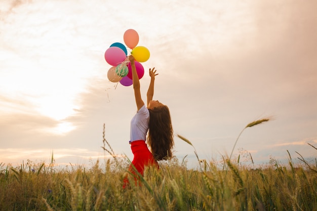 Chica joven con una falda roja con globos de colores en campo de trigo. Inspiración de la naturaleza, luz de fondo