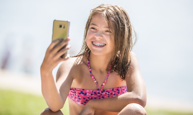 Chica joven feliz con aparatos dentales haciendo selfie en la playa en un día caluroso de verano.