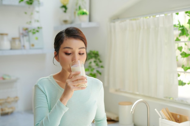 Chica joven feliz bebe una leche para el desayuno en la cocina conner