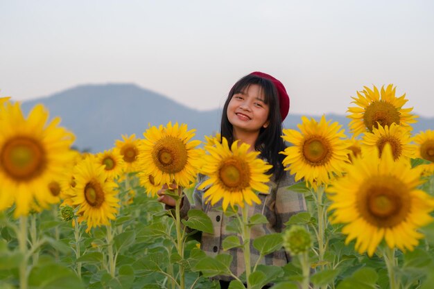 Chica joven feliz en el campo de girasol con cielo azul