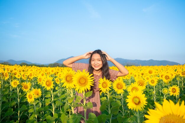 Chica joven feliz en el campo de girasol con cielo azul