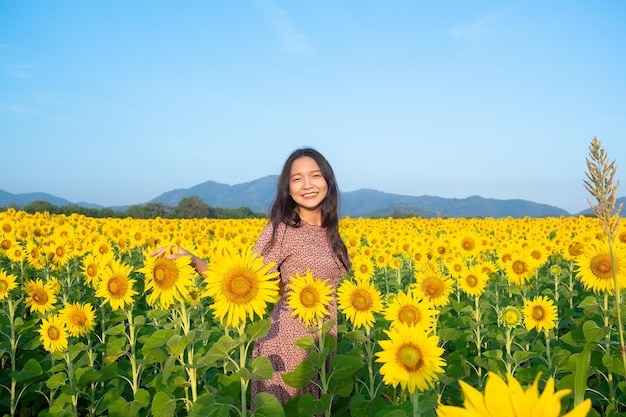 Chica joven feliz en el campo de girasol con cielo azul